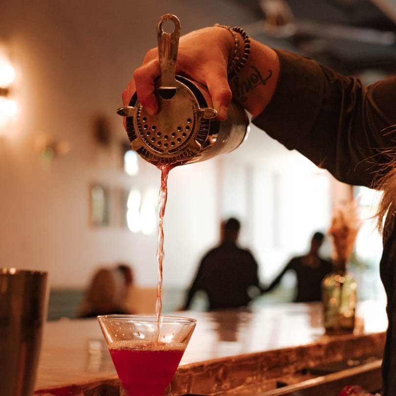 A bartender pours a red cocktail from a shaker into a martini glass at Caffè REL.