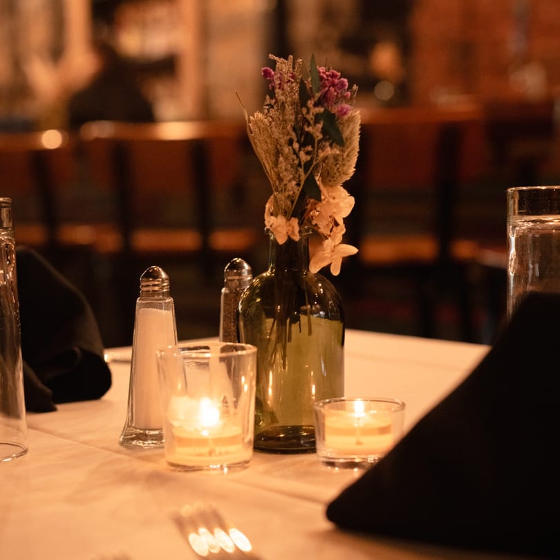 A French restaurant table set with candles, a floral centerpiece, salt, pepper, and water glasses.
