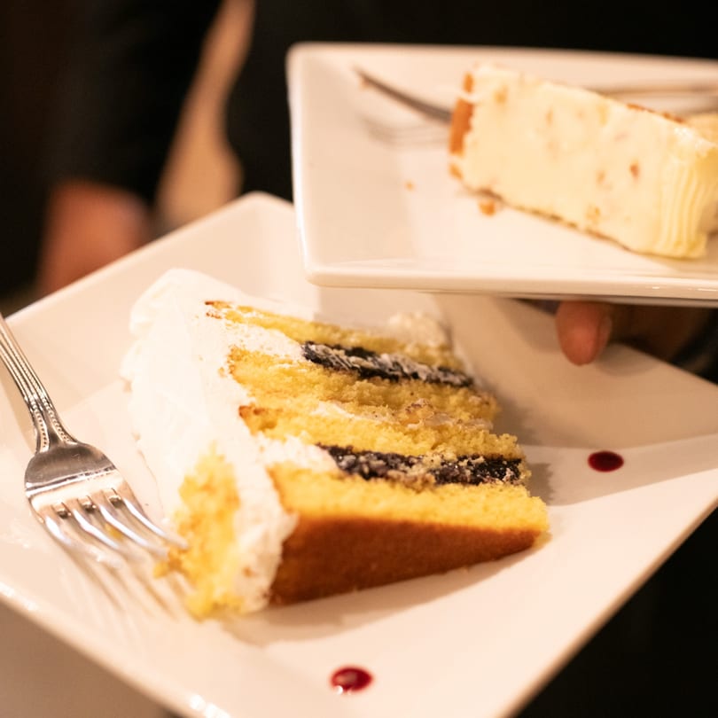 Two slices of cake on white plates, one vanilla with berry filling, the other a creamy dessert.